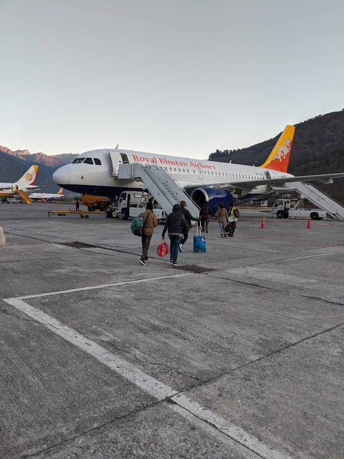 Passengers boarding a Royal Bhutan Airlines Airbus A319 at Paro Airport against mountain backdrop.