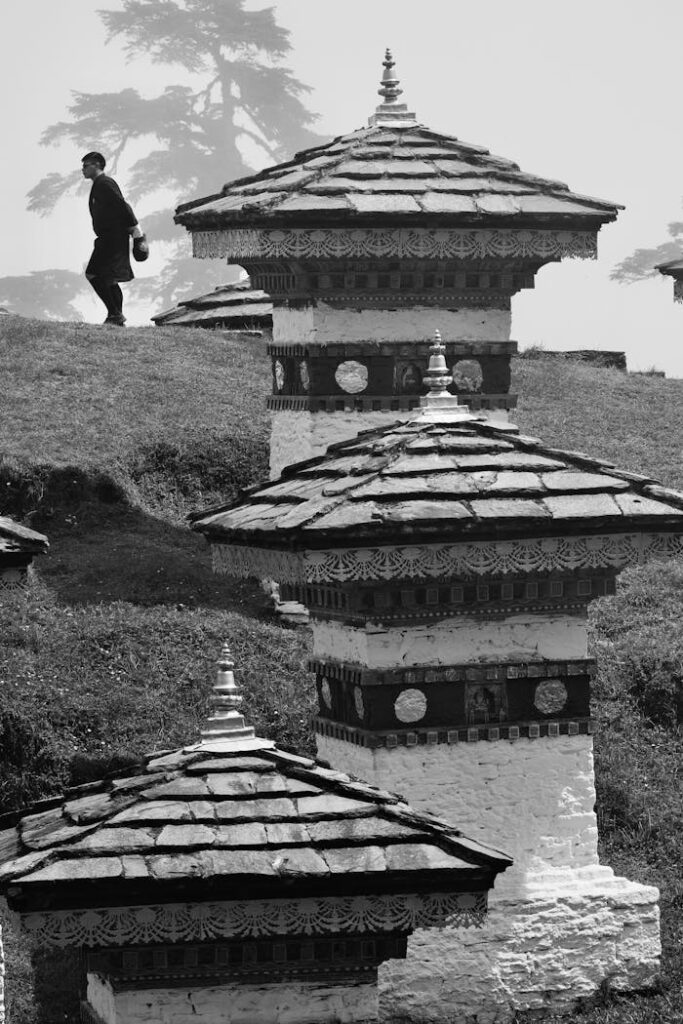 Black and white scene of a person walking among Bhutanese stupas, highlighting traditional architecture.