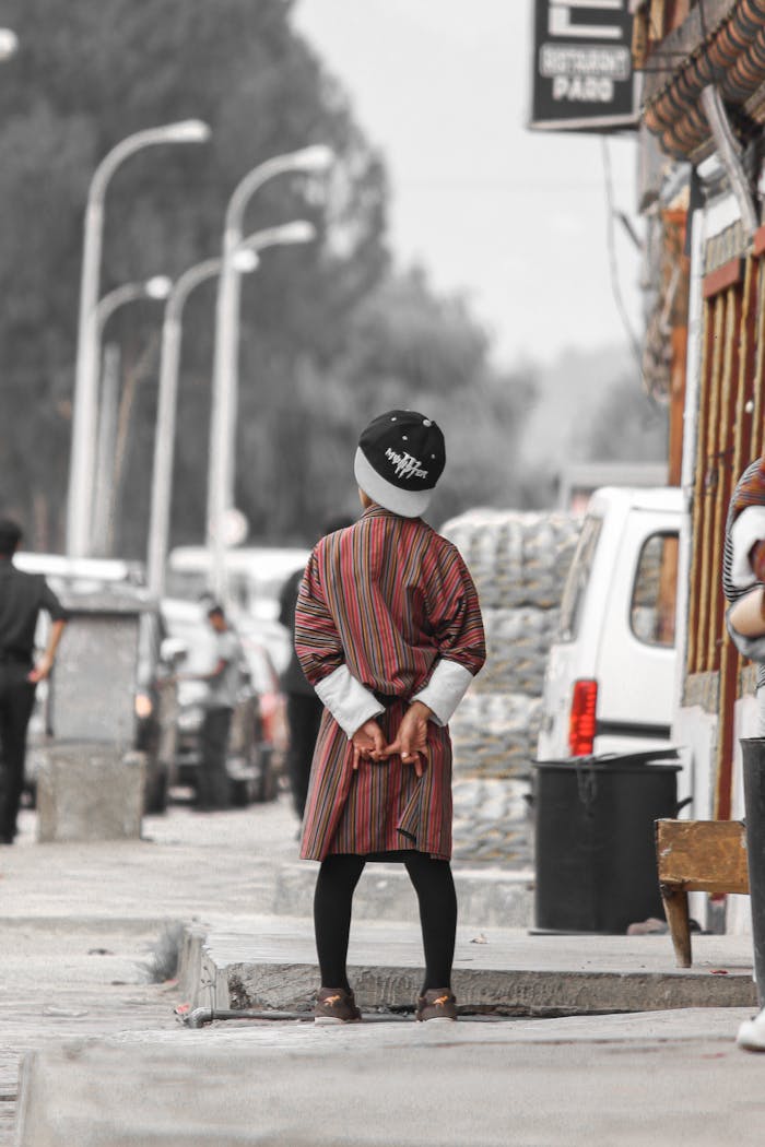A child stands on a Bhutanese street wearing a gho, showcasing cultural attire and urban life.